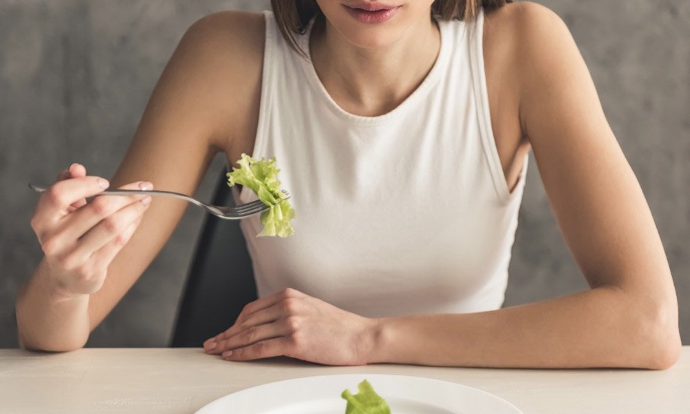 A woman holding up a piece of salad hesitantly